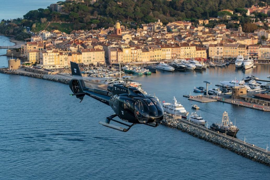 A helicopter flying over Saint-Tropez with the port and its yachts visible in the background.